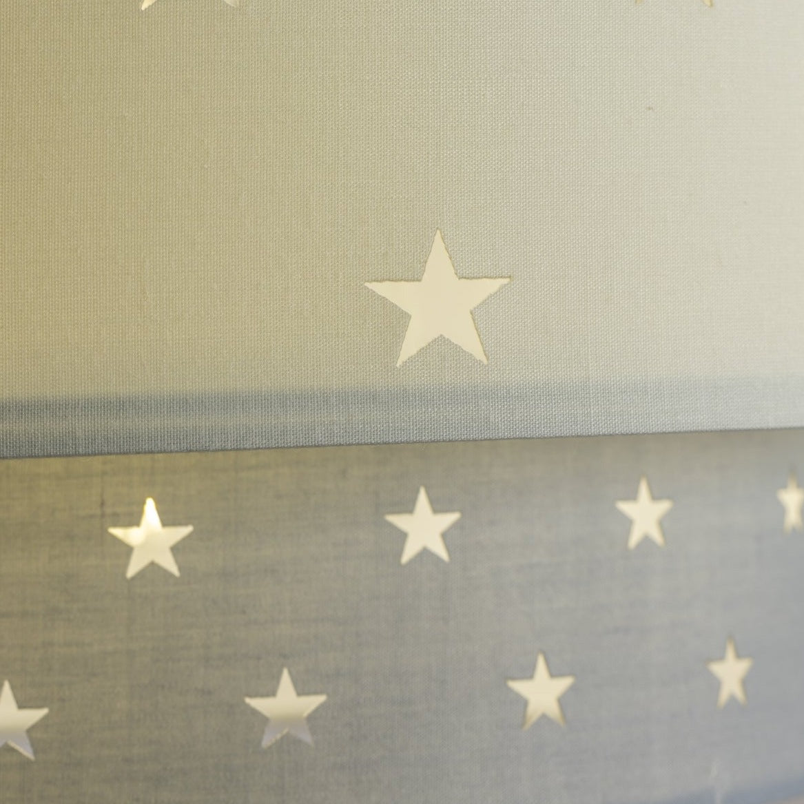 Our Grey and Cream two tiered star shade features a mixture of large and small sweet stars cut out across a grey and cream background. When your lamp is turned on it will shine out through these cut-outs, mimicking a beautiful night sky. This lampshade is made with soft-touch fabric for a little bit of luxury.